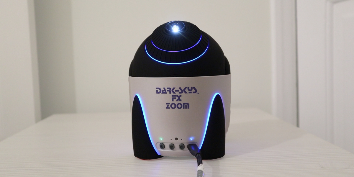 A small, futuristic gadget labeled "Dark Sky FX Zoom" on a table, emitting blue light from its top and sides.